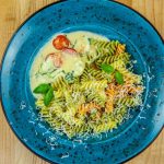 Colorful rotini pasta with cheese and tomatoes on a vibrant blue plate.